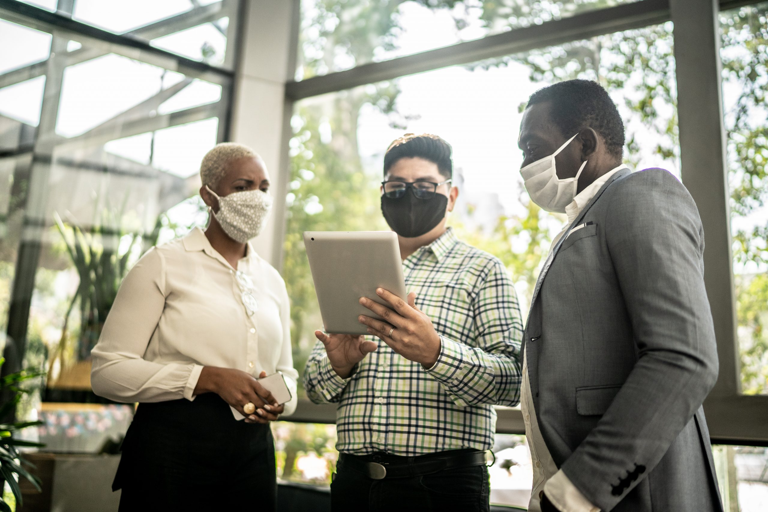 Coworkers on a business meeting using laptop at office's lobby - with face masks on.