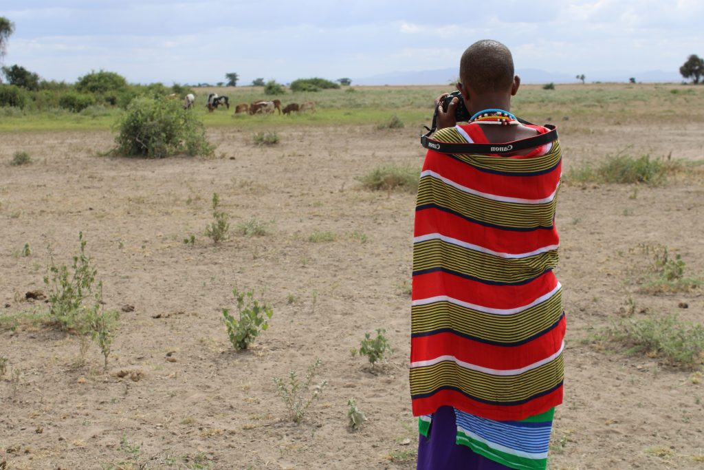 A photography mentee, Catherine Pilalei, points her camera at livestock at a distance during a practical training session at a workshop on climate change adaptation and planning in Amboseli, Kenya. Lensational/ Esther Tinayo (Amboseli Trainee)