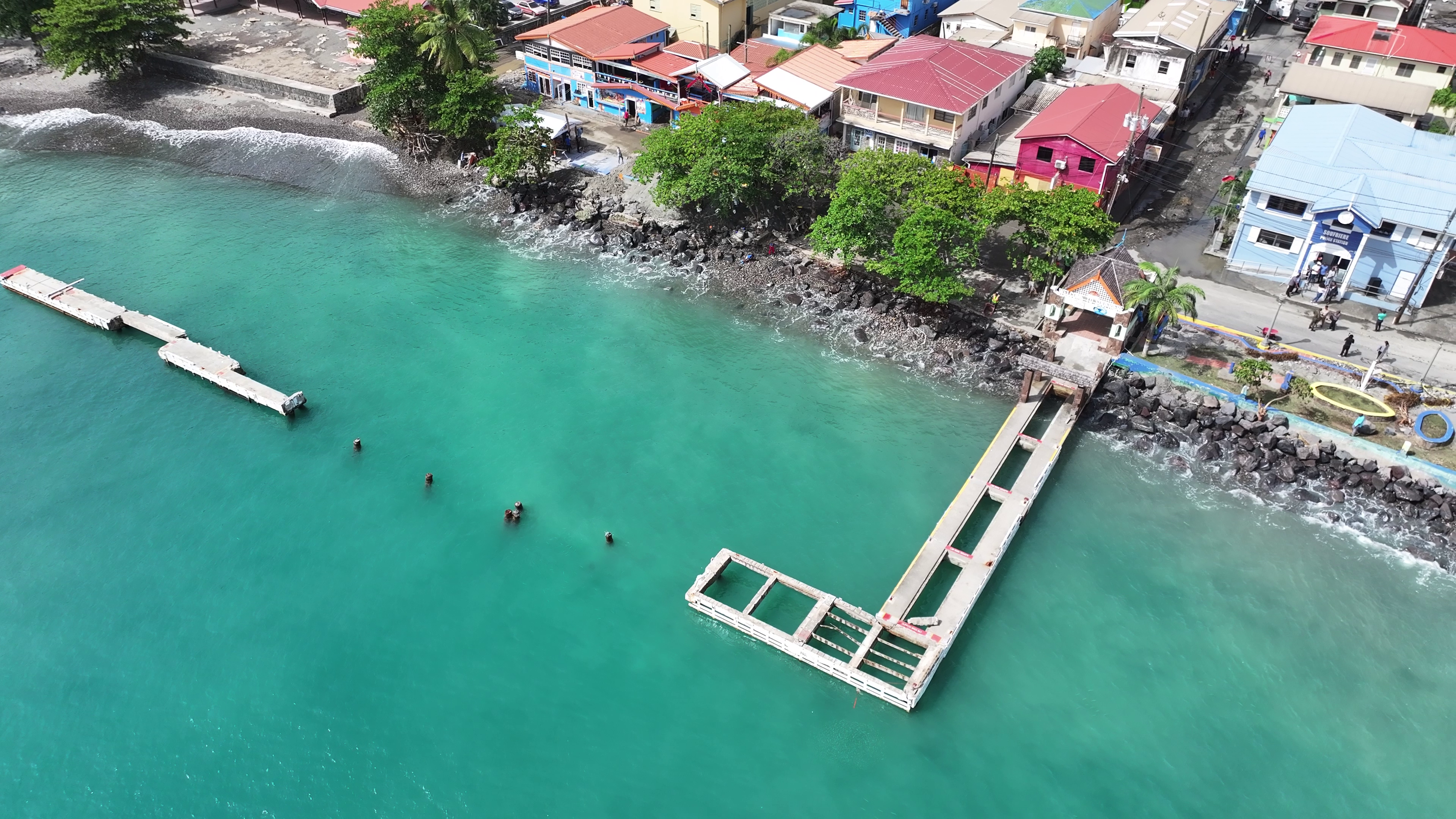 Aerial view of a coastal town with colorful buildings along the shoreline and a small pier extending into turquoise water