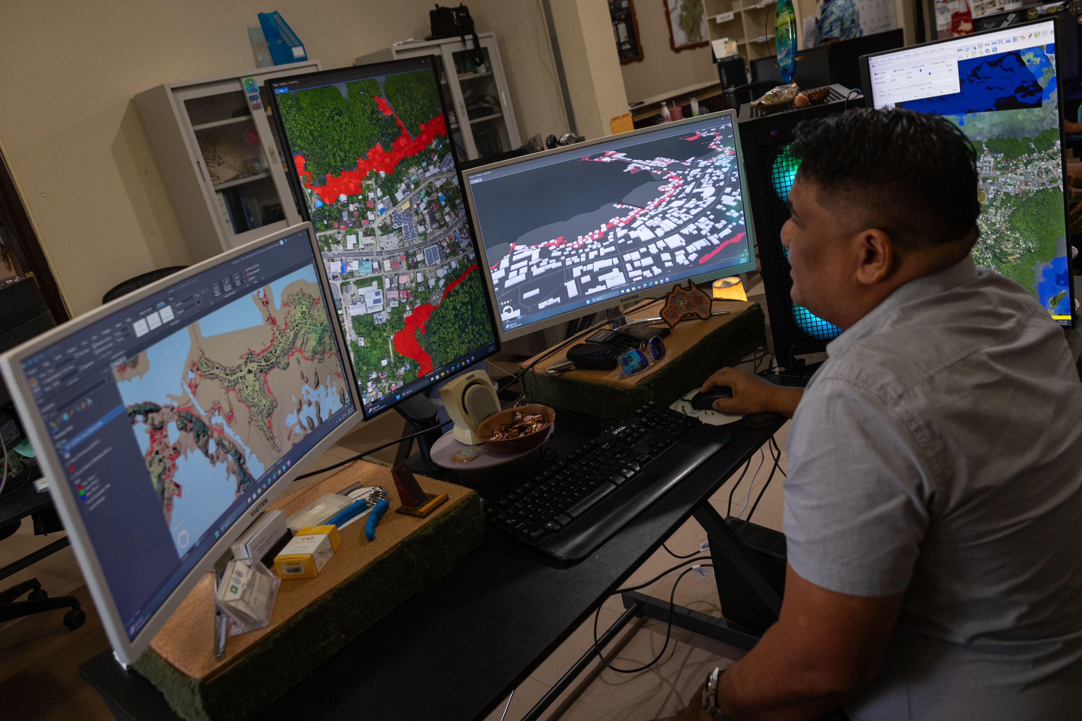 A man sits at a desk in front of 3 computer screens. 